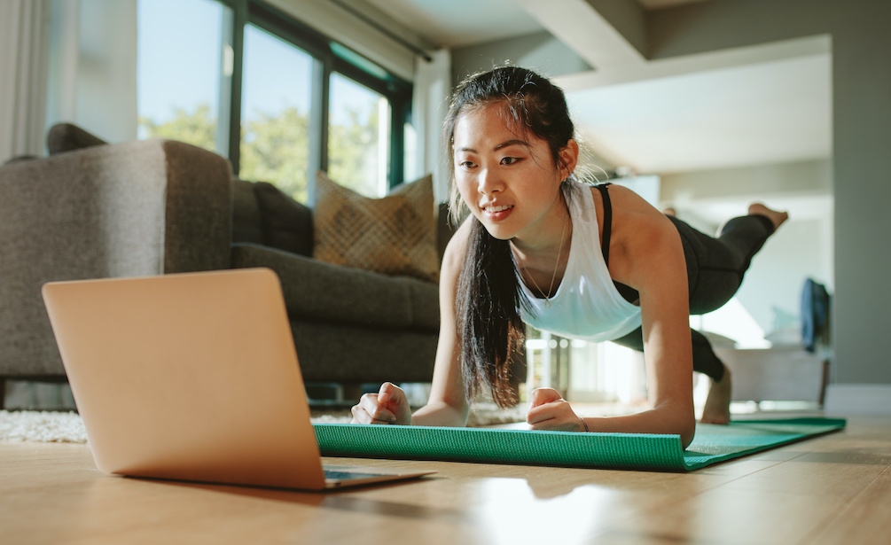 Woman doing one-legged plank watching laptop